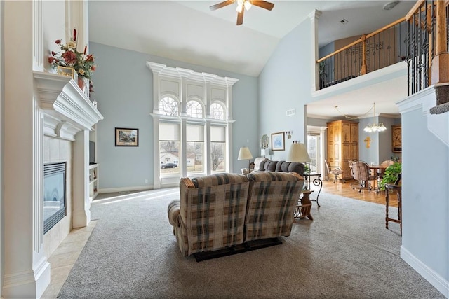 living room with a tile fireplace, ceiling fan with notable chandelier, light colored carpet, and high vaulted ceiling