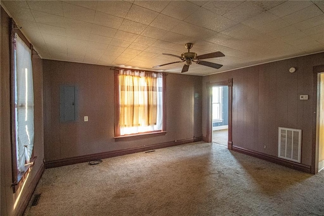 carpeted spare room with ceiling fan, electric panel, and wood walls