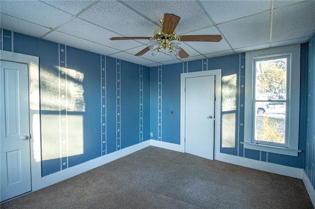 empty room featuring ceiling fan, a drop ceiling, and carpet flooring