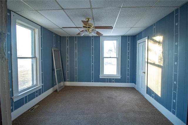 carpeted spare room with ceiling fan and a drop ceiling