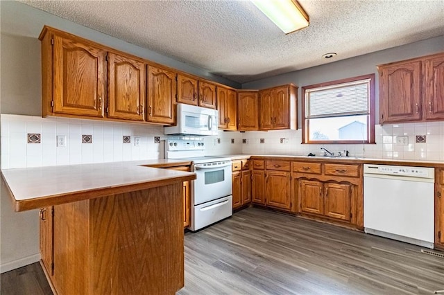 kitchen with tasteful backsplash, white appliances, kitchen peninsula, a textured ceiling, and light wood-type flooring