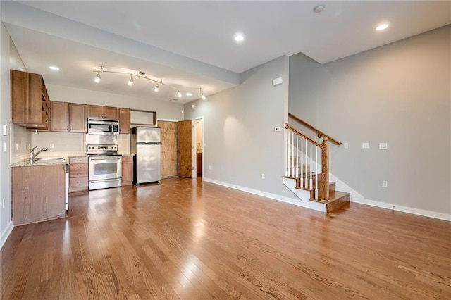 kitchen featuring baseboards, light wood-type flooring, a sink, appliances with stainless steel finishes, and brown cabinets