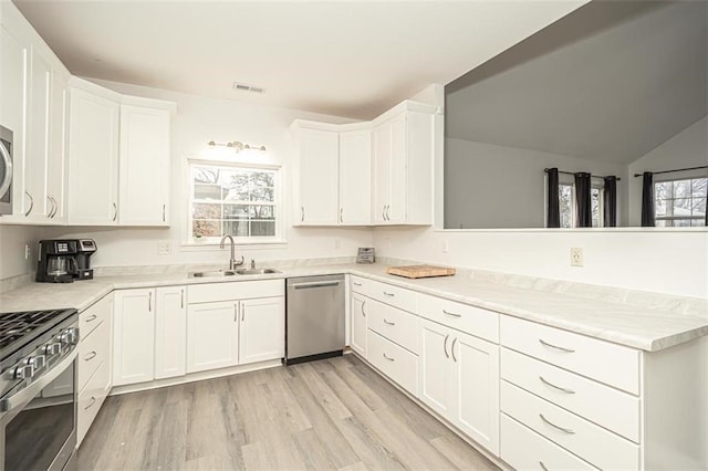 kitchen with light wood-type flooring, appliances with stainless steel finishes, sink, and white cabinetry