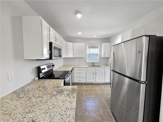 kitchen with white cabinetry, appliances with stainless steel finishes, tile patterned floors, light stone counters, and sink