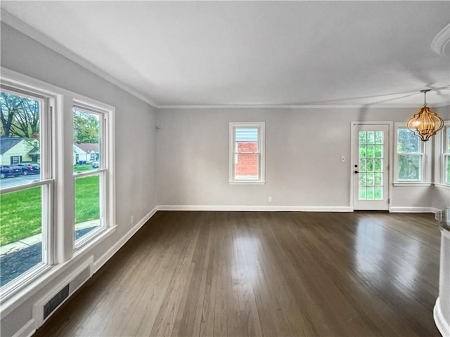 spare room with a wealth of natural light, dark hardwood / wood-style floors, crown molding, and an inviting chandelier