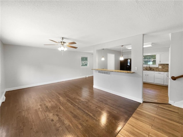 unfurnished living room with ceiling fan, sink, a wealth of natural light, and dark hardwood / wood-style floors