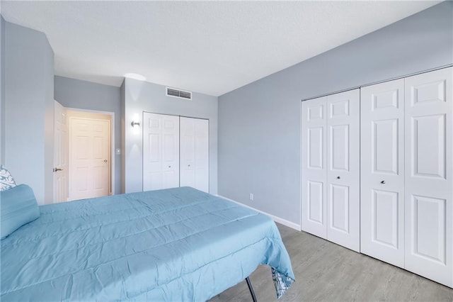 bedroom with multiple closets and light wood-type flooring