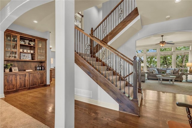 staircase featuring visible vents, a towering ceiling, ceiling fan, wood finished floors, and baseboards