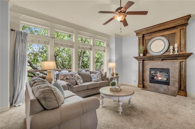 carpeted living area featuring ceiling fan, a tiled fireplace, baseboards, and crown molding