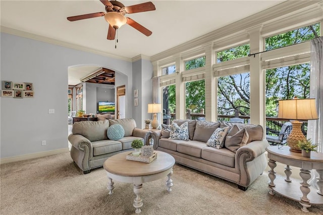 living area with arched walkways, a ceiling fan, baseboards, ornamental molding, and carpet