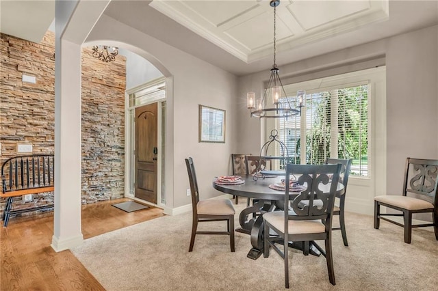 dining space featuring light wood finished floors, a chandelier, a raised ceiling, and arched walkways