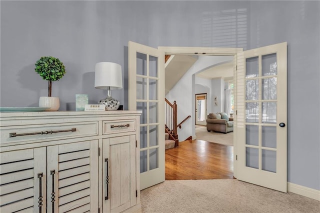 interior space with arched walkways, french doors, and light carpet