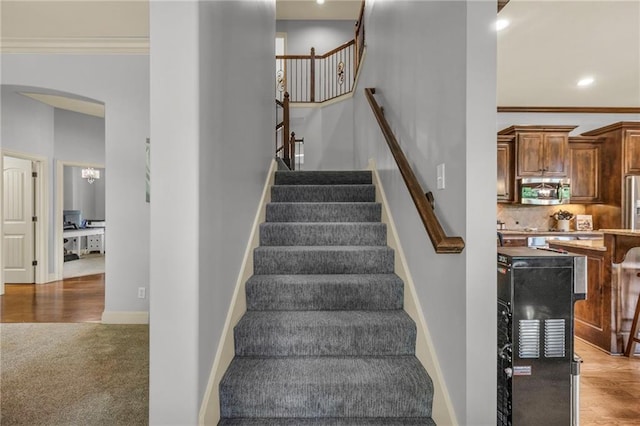 stairway with baseboards, arched walkways, crown molding, and carpet flooring