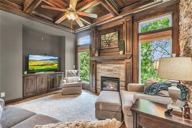 living area with ornamental molding, a glass covered fireplace, coffered ceiling, and baseboards