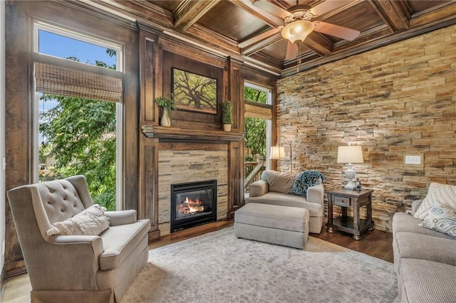 living area with coffered ceiling, wood finished floors, ornamental molding, beamed ceiling, and a tiled fireplace