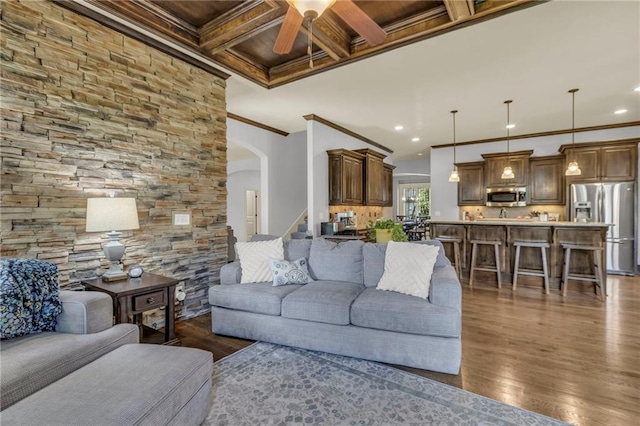 living room with dark wood-style floors, ornamental molding, arched walkways, and a ceiling fan