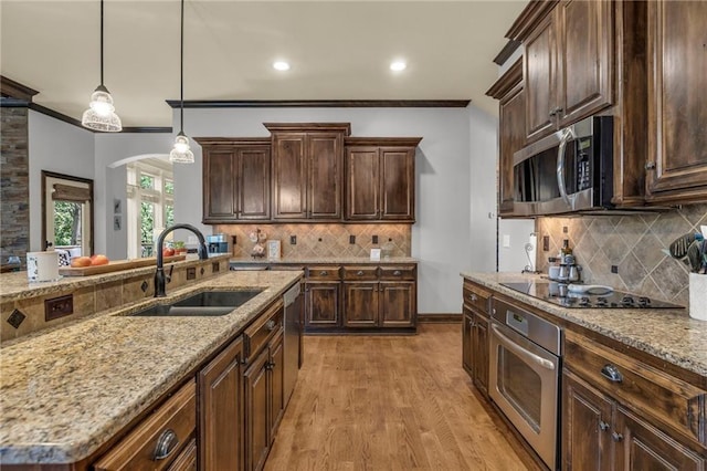 kitchen featuring arched walkways, a sink, appliances with stainless steel finishes, decorative light fixtures, and crown molding