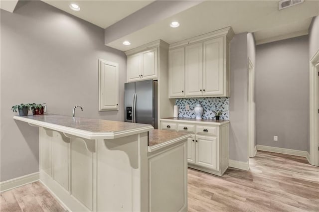 kitchen featuring a breakfast bar, visible vents, light countertops, a peninsula, and stainless steel fridge with ice dispenser