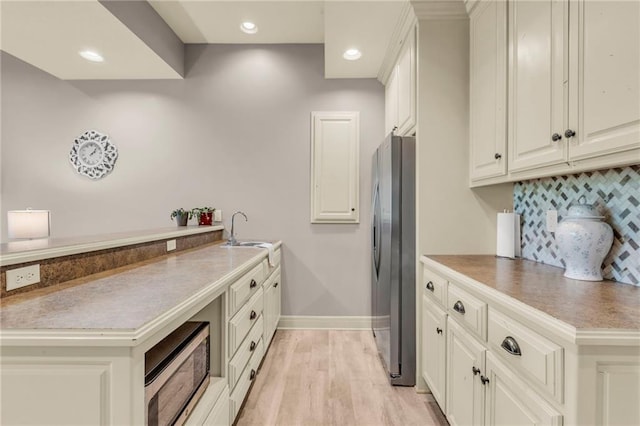 kitchen featuring light wood finished floors, decorative backsplash, appliances with stainless steel finishes, a peninsula, and a sink