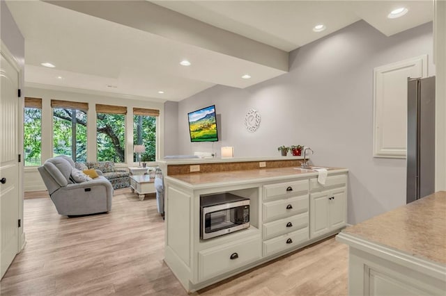 kitchen featuring light wood finished floors, a peninsula, stainless steel appliances, a sink, and recessed lighting