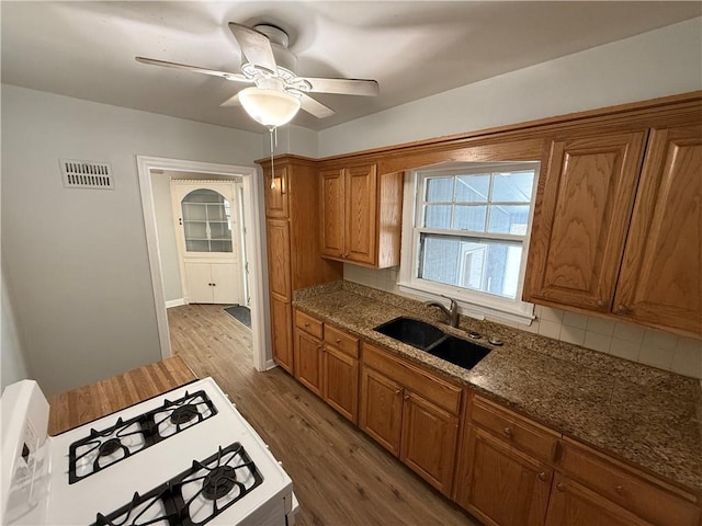 kitchen with light hardwood / wood-style floors, ceiling fan, white range with gas cooktop, dark stone countertops, and sink