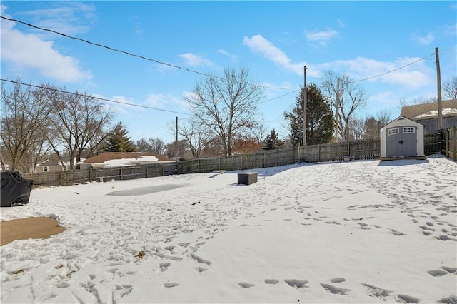 snowy yard featuring a storage shed, an outdoor structure, and a fenced backyard