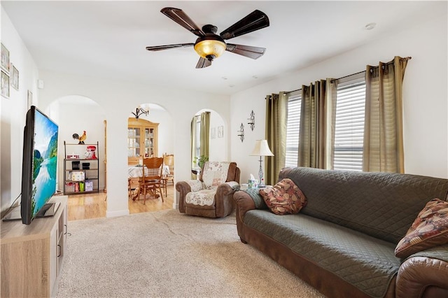 living area featuring ceiling fan, arched walkways, and light colored carpet