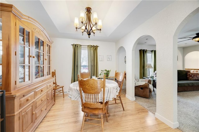 dining area featuring a chandelier, light wood-type flooring, a raised ceiling, and baseboards