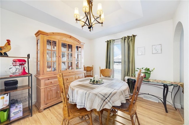 dining space featuring light wood-style flooring, a tray ceiling, a notable chandelier, and arched walkways