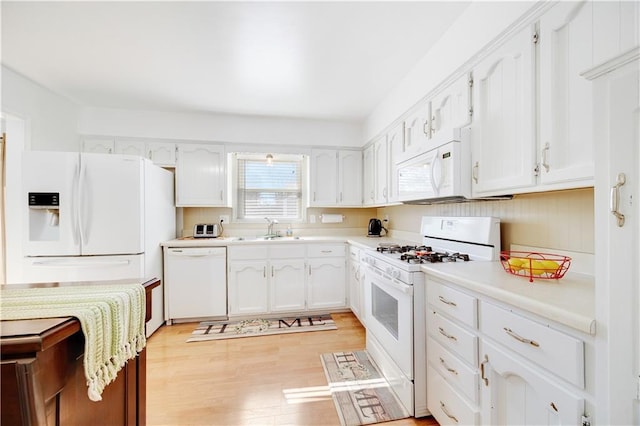 kitchen with white appliances, a sink, white cabinets, light countertops, and light wood-type flooring