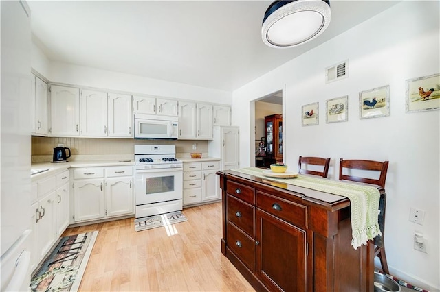 kitchen with white appliances, visible vents, white cabinets, light countertops, and light wood-style floors