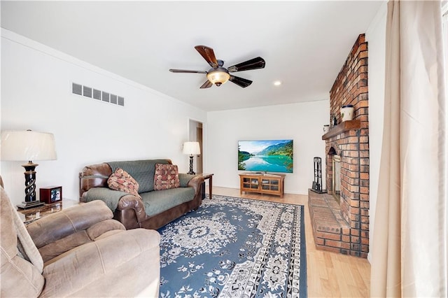 living room featuring a fireplace, crown molding, visible vents, ceiling fan, and wood finished floors