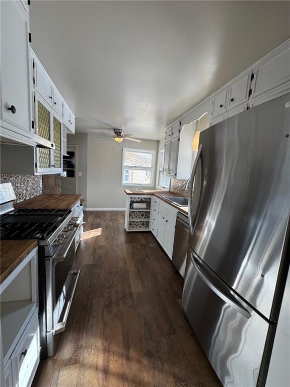 kitchen with appliances with stainless steel finishes, dark wood-type flooring, white cabinetry, decorative backsplash, and ceiling fan