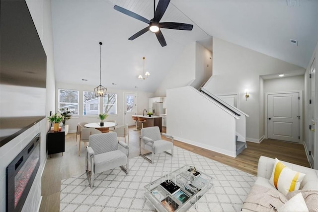 living room featuring high vaulted ceiling, light hardwood / wood-style flooring, and ceiling fan with notable chandelier