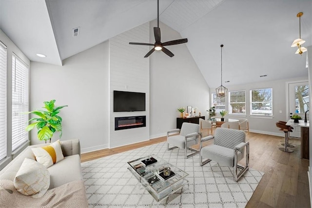 living room with light hardwood / wood-style floors, ceiling fan with notable chandelier, high vaulted ceiling, and a fireplace