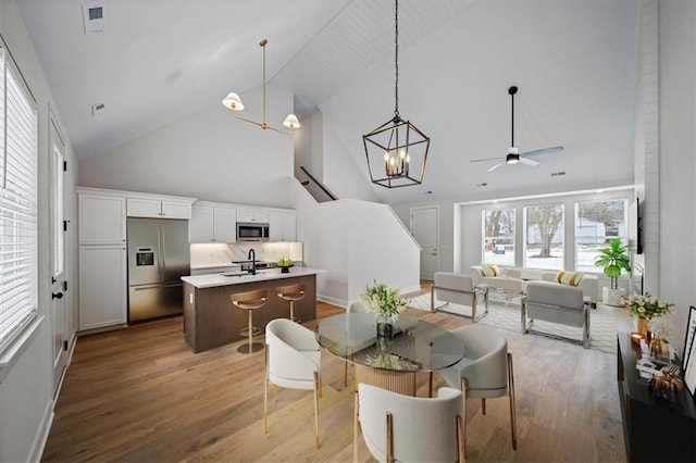 dining room with ceiling fan with notable chandelier, sink, hardwood / wood-style floors, and high vaulted ceiling