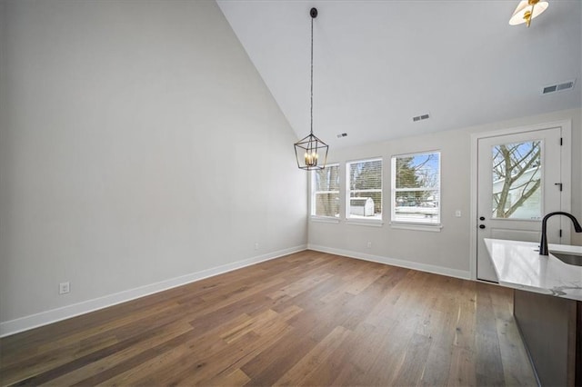 unfurnished dining area featuring dark wood-type flooring, lofted ceiling, an inviting chandelier, and sink