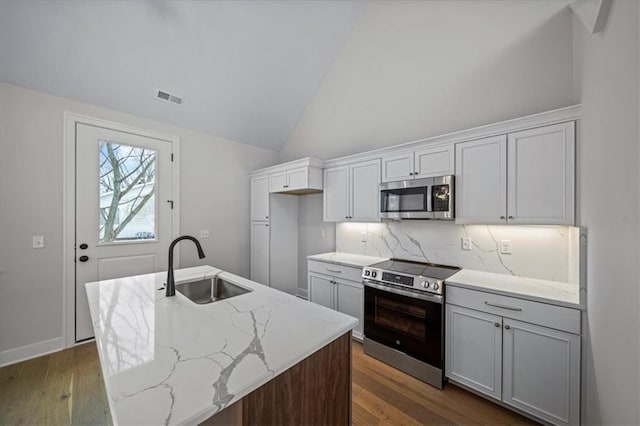 kitchen featuring a center island with sink, appliances with stainless steel finishes, backsplash, light stone counters, and sink