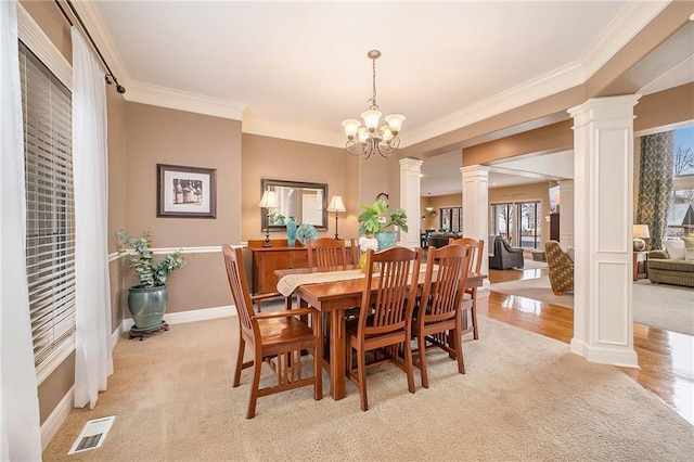 carpeted dining area with decorative columns, ornamental molding, and a notable chandelier