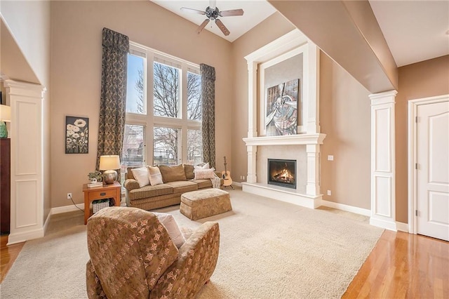 living area with ceiling fan, a towering ceiling, hardwood / wood-style flooring, and ornate columns