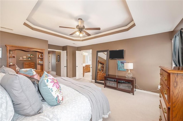 carpeted bedroom with ensuite bathroom, ceiling fan, and a tray ceiling