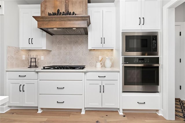 kitchen featuring built in microwave, premium range hood, stainless steel oven, white cabinets, and black gas cooktop