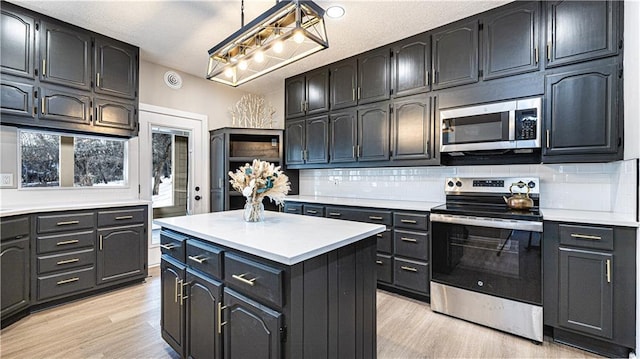 kitchen with appliances with stainless steel finishes, a kitchen island, tasteful backsplash, hanging light fixtures, and light hardwood / wood-style flooring