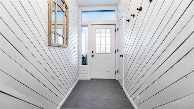 doorway with dark tile patterned floors and wood walls