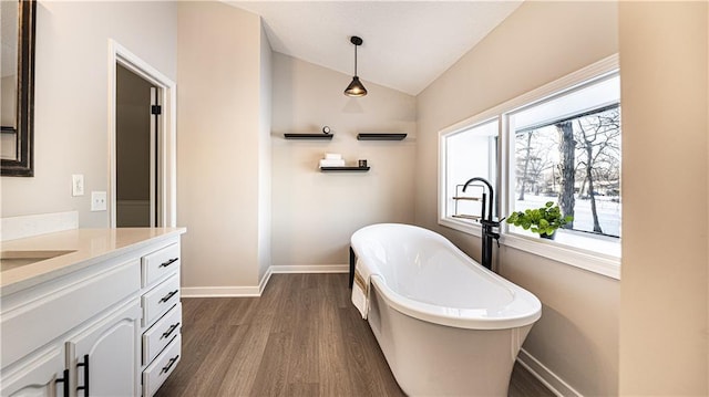 bathroom featuring vaulted ceiling, hardwood / wood-style flooring, a tub, and vanity