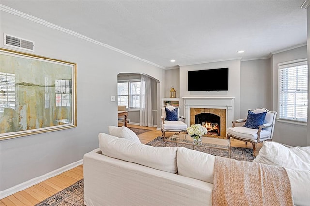 living room with crown molding, a fireplace, and light wood-type flooring