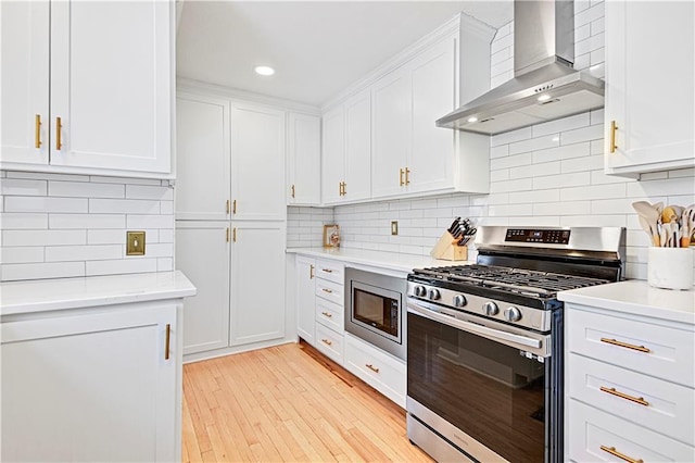 kitchen with white cabinetry, stainless steel appliances, light hardwood / wood-style floors, decorative backsplash, and wall chimney exhaust hood