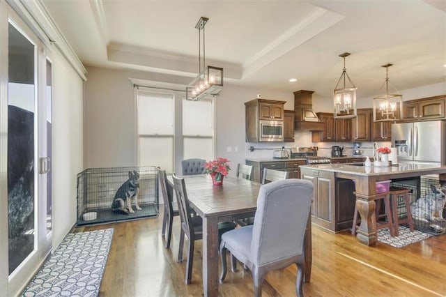 dining area with plenty of natural light, a raised ceiling, sink, and light wood-type flooring