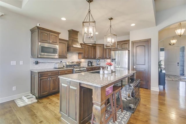 kitchen featuring a breakfast bar, sink, appliances with stainless steel finishes, custom range hood, and a kitchen island with sink