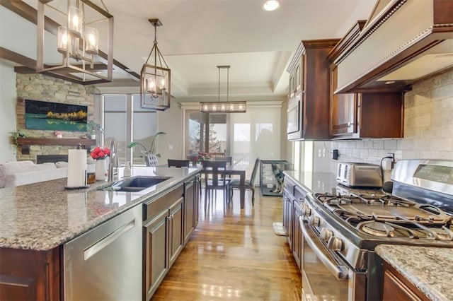 kitchen with premium range hood, sink, decorative light fixtures, stainless steel appliances, and light stone countertops